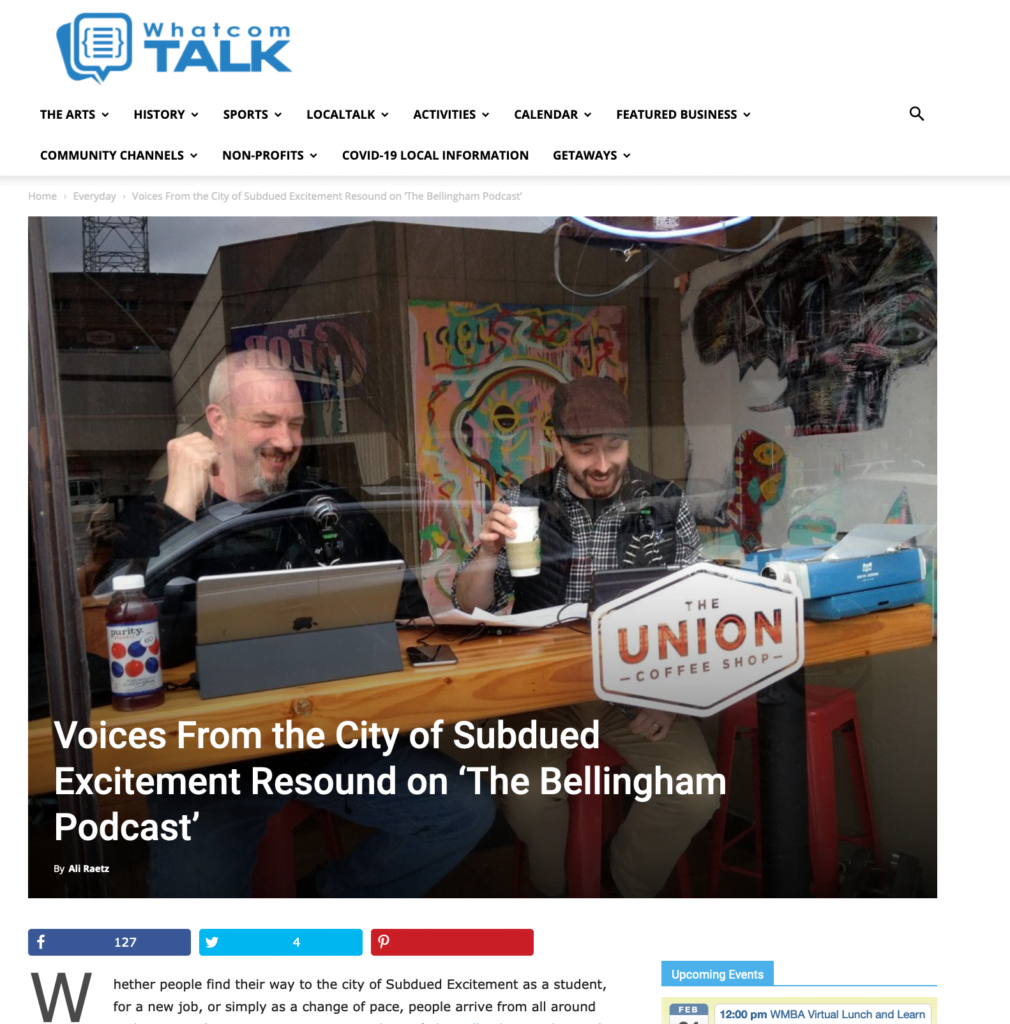 Cover shot of Whatcom Talk article with Chris Powell and AJ Barse laughing behind a coffee shop window (Union Coffee) with devices, mics, and a typwriter infront of them